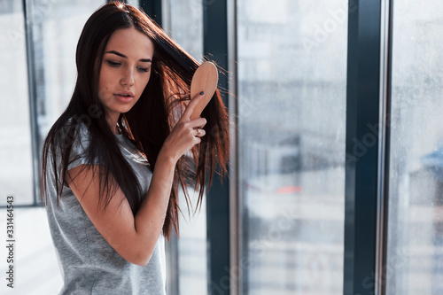 Beautiful young brunette in grey shirt standing near window and posing for a camera Free Download Beautiful young brunette in grey shirt standing near window and posing for a camera - GFXLoad