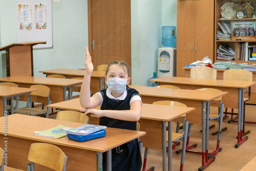 Girl schoolgirl in a protective medical mask sits alone in a school class. The concept of a virus epidemic and distance learning for children. Quarantine