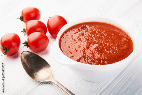 Tomato soup in a white bowl and fresh tomatoes on the table
