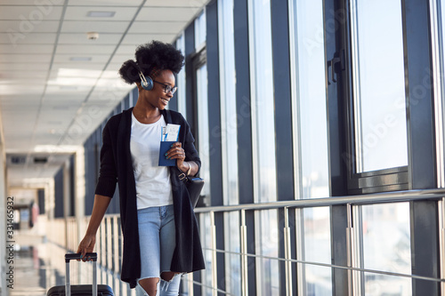 Young african american female passanger in casual clothes and headphones is in airport with baggage