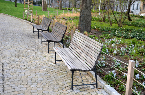 wooden park bench with metal structure on granite pavement in the park supporting wall of rope fences shrub and perennial flower beds