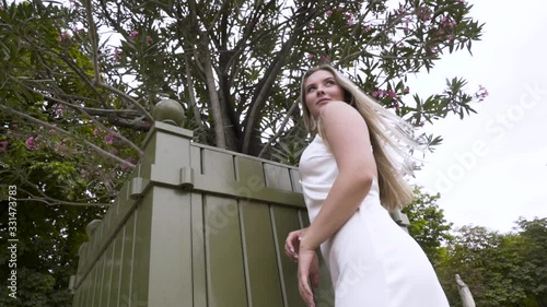 Young pretty sexy caucasian woman in white dress in a blooming spring garden. Action. Youth, freshness, beauty, romance, happiness concept, bottom view of blond model shaking her head and touching her photo