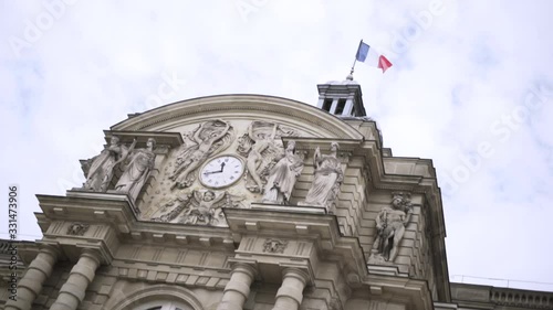 French flag waving in the wind on a historic building, architecture concept. Action. Bottom view of a beautiful old building with sculptures and clock. photo