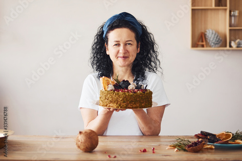Senior woman with black curly hair holding dietical cake on kitchen