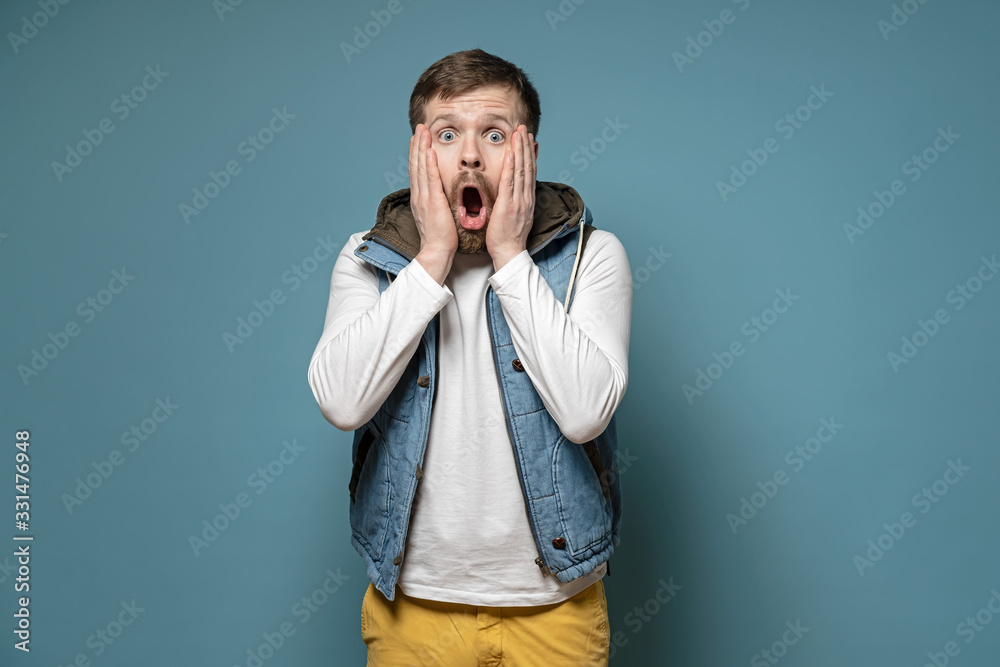 Handsome, bearded man is surprised, he does not believe what he saw, put hands on cheeks and in shock opened mouth. Handsome, bearded man is surprised, he does not believe what he saw, put hands on cheeks and in shock opened mouth.