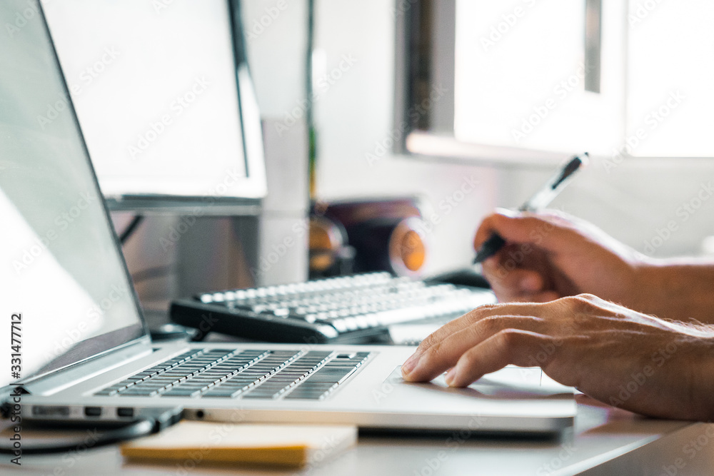 Person holding a pen working from home at their desk with computers Person holding a pen working from home at their desk with computers