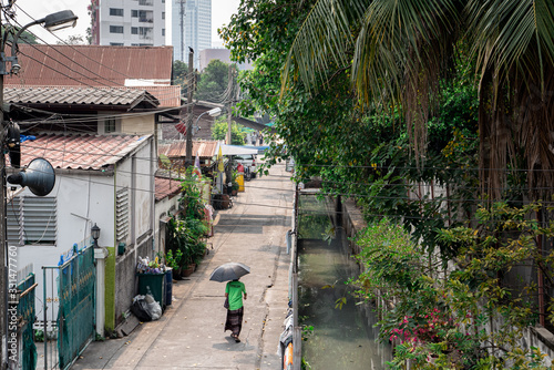Woman walking along houses and Khlong, slum in Bangkok, Thailand