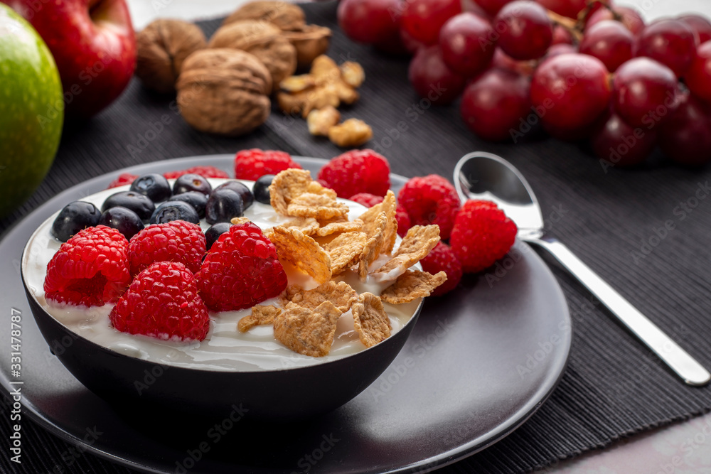 Healthy breakfast in bowl with yogurt and berries and cereals surrounded by apples, nuts and grapes.