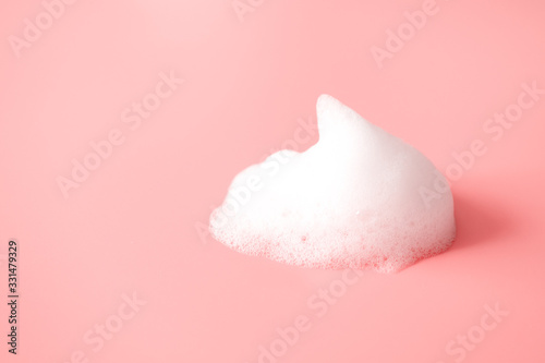 White foam snear from soap, shampoo or cleanser on pink background with selective focus. Close-up, macro photo