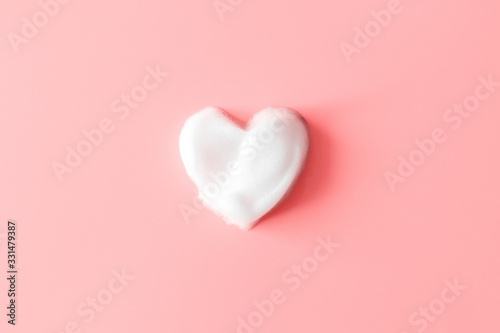 Heart from soap foam on pink background. White cleanser texture. Concept hygiene and healthcare