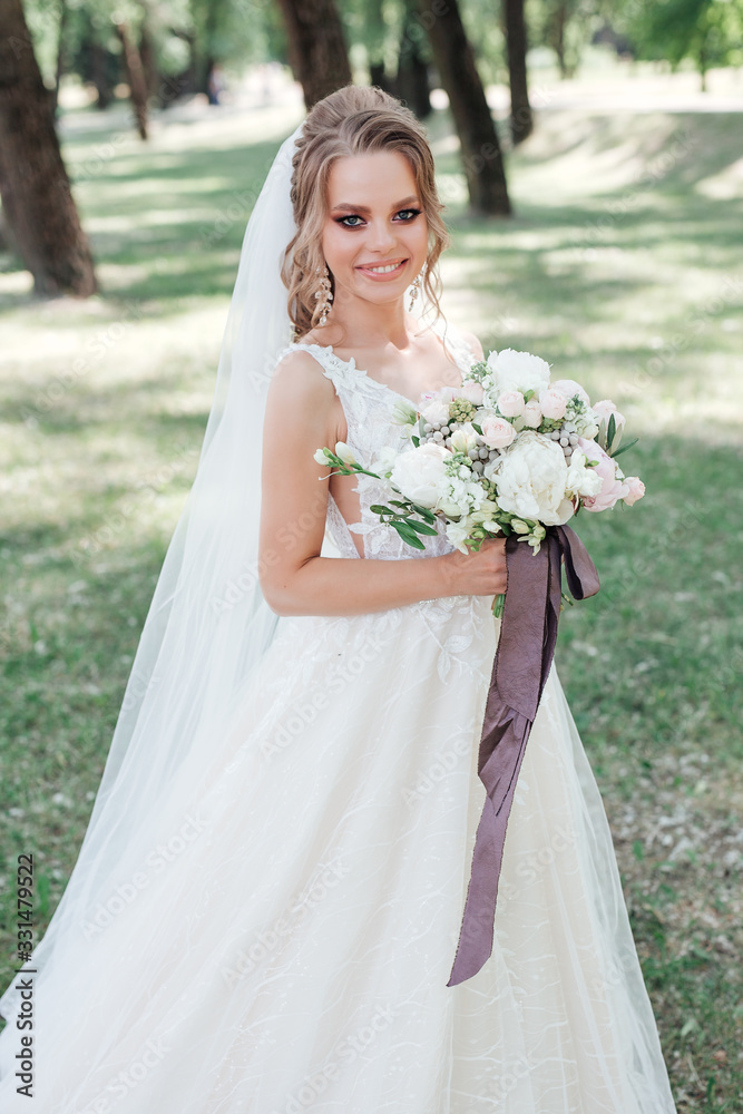 Stunning young bride holding wedding bouquet and smiling at camera outdoor
