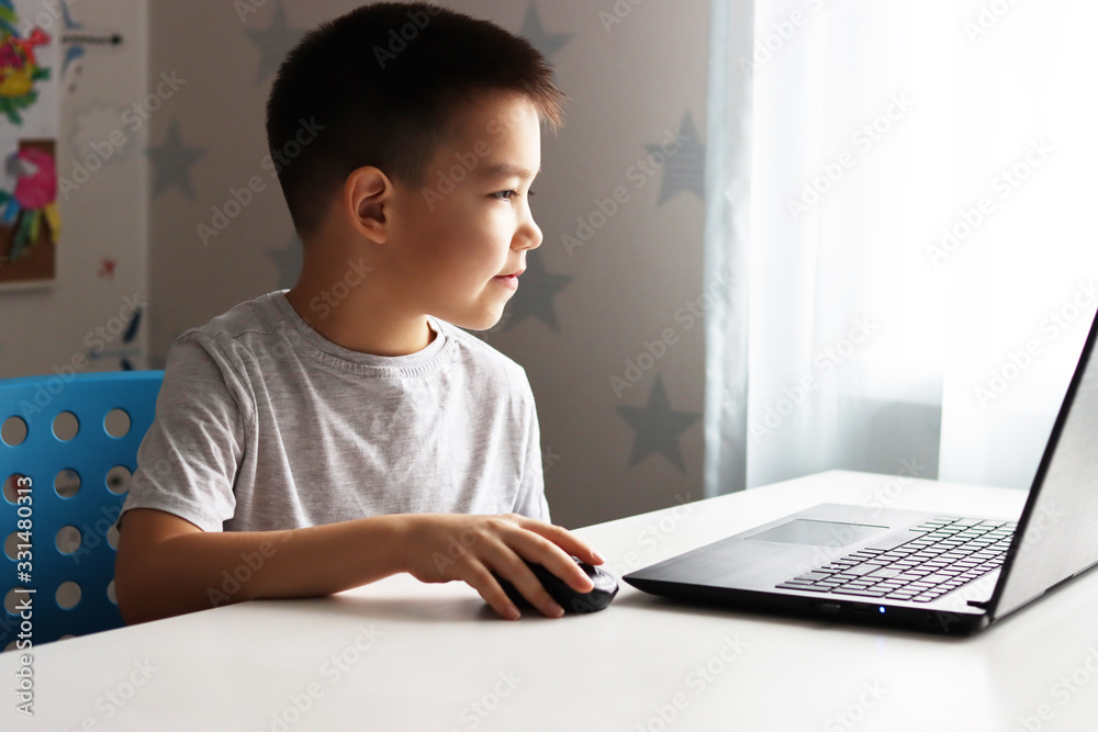a small boy Samir is sitting at a table playing on the computer and phone a small boy Samir is sitting at a table playing on the computer and phone