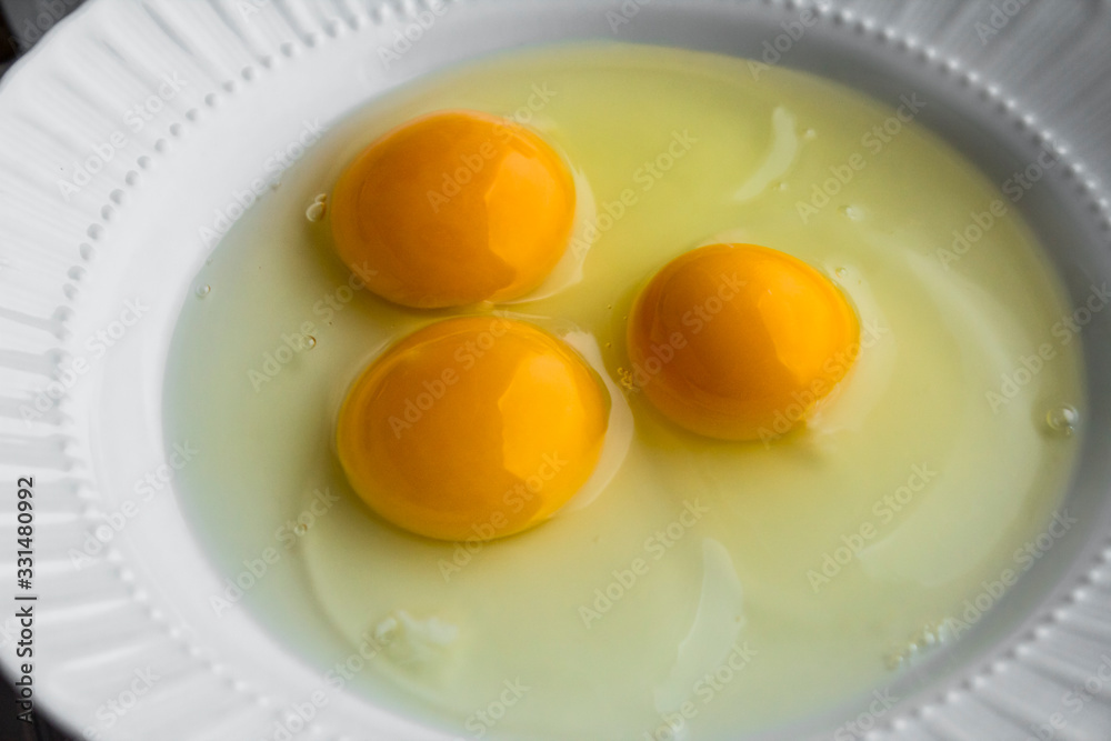Three broken eggs on the white porcelain plate.Preparing to cook omelette.Above view Three broken eggs on the white porcelain plate.Preparing to cook omelette.Above view
