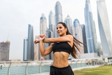 Young fitness woman make warming hands exercises before run against skyscrapers background