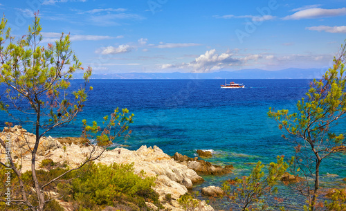 Greece Sithonia Chalkidiki near paradise beach with rock and pine-tree. Scenic landscape Aegean sea and white ship at blue wave.