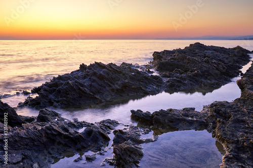 Sunset at sea with black volcanic rocks and pink sky. Picturesque landscape sunrise.