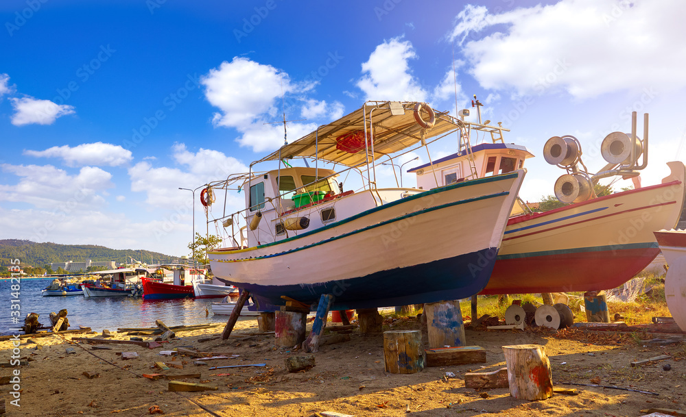 Fishing wooden boats in dock station for repair ships. Greece Sithonia Chalkidiki. Picturesque sunny day with blue sky and white clouds. Fishing wooden boats in dock station for repair ships. Greece Sithonia Chalkidiki. Picturesque sunny day with blue sky and white clouds.