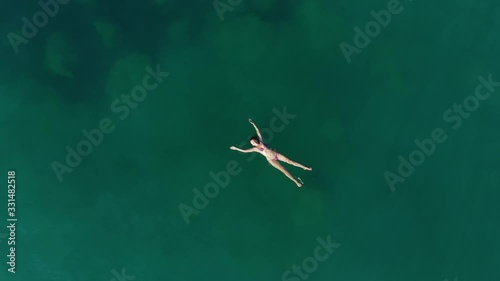 Relaxed woman lie on sea water with arms and hands stretched out, camera fly up, nobody around. Warm and calm waters of Aegean Sea, female swimmer take rest photo