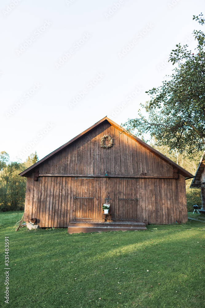 Obraz premium Stylish wooden barn in countryside, on green grass. Summer sunset. Wooden barn in rural area, summer sunset view