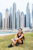 Young woman runner resting after workout outdoors in the skyscrapers background. Female jogger taking a break from running workout.