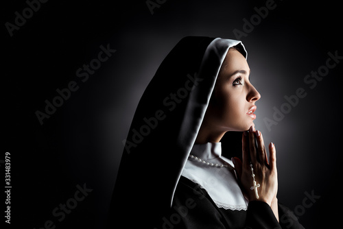 beautiful young nun looking up while praying with cross on grey