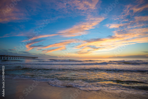 sunset sky and clouds over ocean waves at beach with pier in background