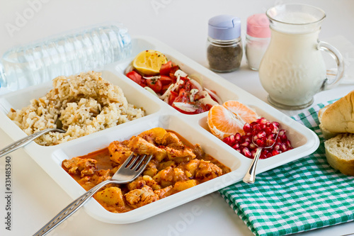 Traditional Turkish Meal with chicken potato,rice,tomato salad and fruits in the white portion food tray.Table d'hote-known TABLDOT in TR-Designed on the white surface.