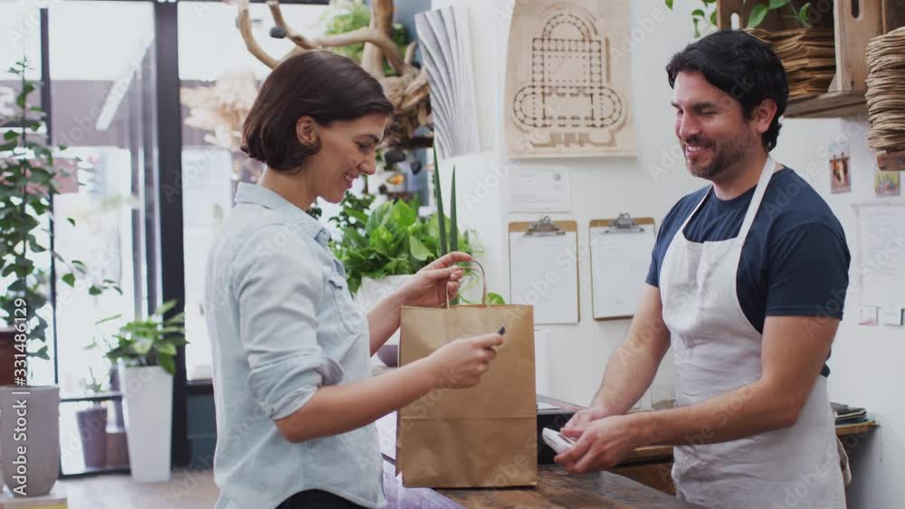 Woman in florists shop making contactless payment at sales desk - shot in slow motion