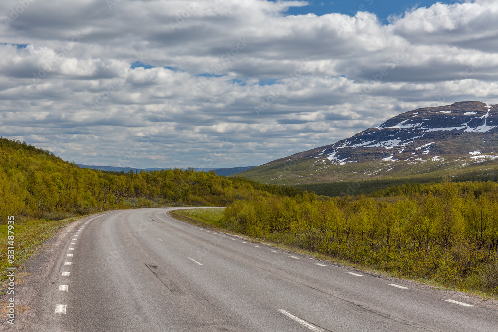 straight and lonely road between swedish mountains under cloudy sky, selective focus, Swedish mountains border with norway. snow peaks