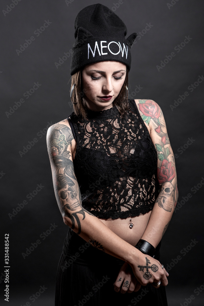 Ragazza tatuata con cuffietta indossa una canotta nera ,e posa con aria seria isolata su sfondo nero Ragazza tatuata con cuffietta indossa una canotta nera ,e posa con aria seria isolata su sfondo nero