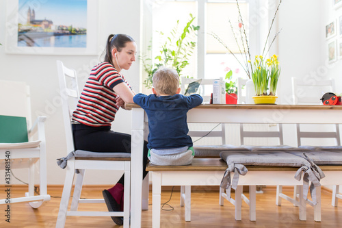 Mutter passt auf Sohn auf und arbeitet im Home Office während der Corona Krise und Covid 19 und Ausgangssperre