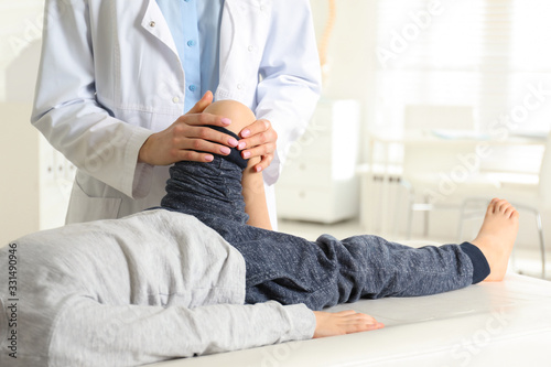 Professional orthopedist examining little patient's leg in clinic photo