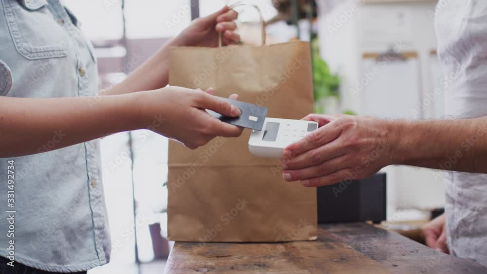 Close up of woman in store making contactless payment at sales desk holding card to reader - shot in slow motion Close up of woman in store making contactless payment at sales desk holding card to reader - shot in slow motion