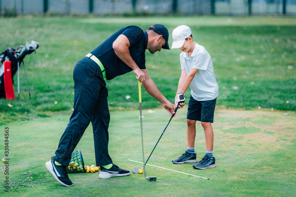 Obraz premium Golf Lessons. A golf Instructor and a boy practicing on a Golf Practice Range