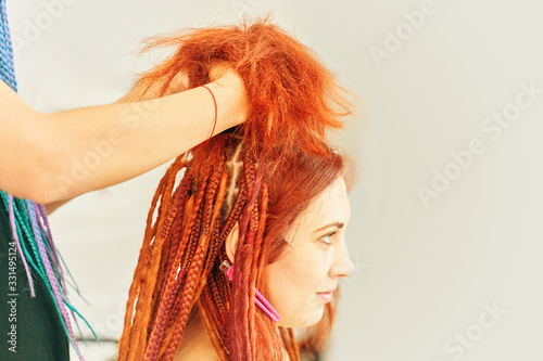 Barber braids de dreadlocks. The hairdresser weaves braids with red kanekalons beautiful red-head beauty salon. kanekalon photo