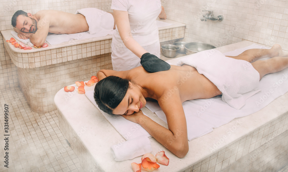 Mixed race woman having skin peeling in turkish hammam while her boyfriend  enjoys the warmth of a Turkish bath marble massage table Photos | Adobe  Stock