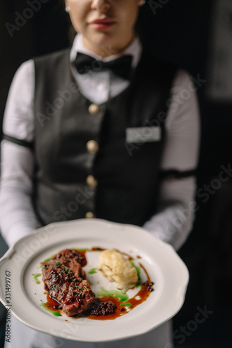 Waitress holding beef steak with potatoes gratin and green sauce on a plate. Smooth image with shallow depth of field.