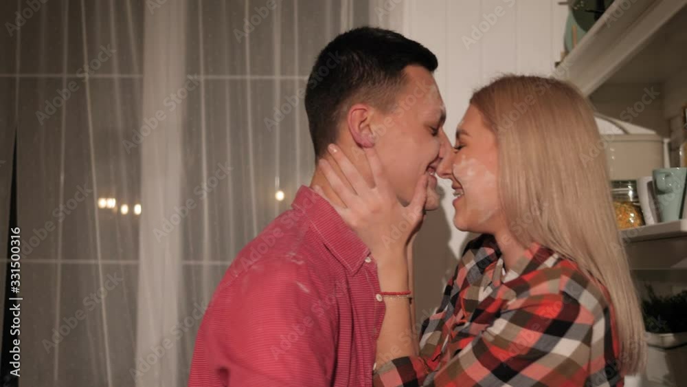 Close-up couple with soiled flour faces kissing and cuddling in the kitchen in the evening. A couple in love spends a date at home in the kitchen. Slow motion. Close-up couple with soiled flour faces kissing and cuddling in the kitchen in the evening. A couple in love spends a date at home in the kitchen. Slow motion.
