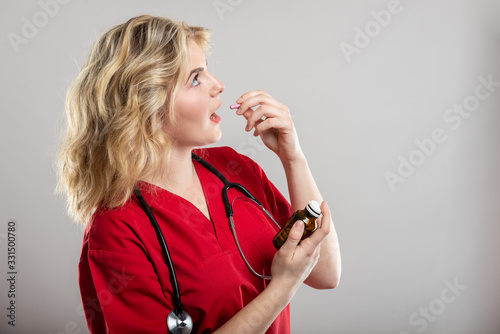 Portrait of female nurse wearing red scrub taking one pill