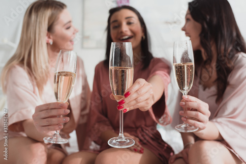 Selective focus of multiethnic women holding champagne glasses and smiling at bachelorette party