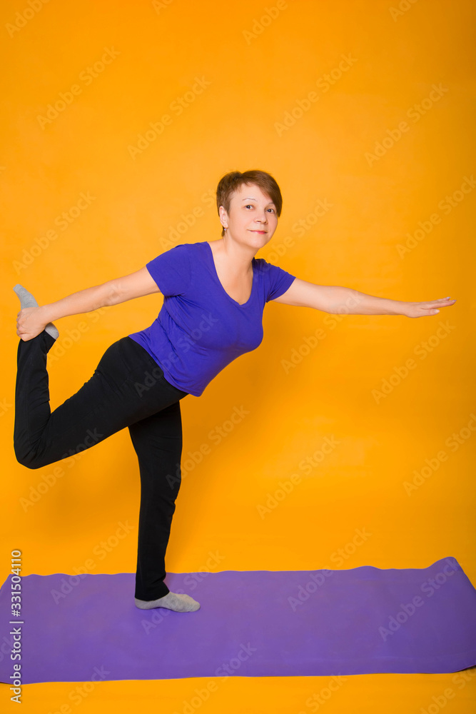 Woman at the age of doing yoga standing on a yellow background.