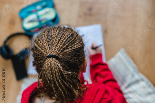junges Mädchen mit geflochtenen Haare, open braids, liegt auf Holzfußboden und rechnet, macht Hausaufgaben. selektive Schärfe © Sonja