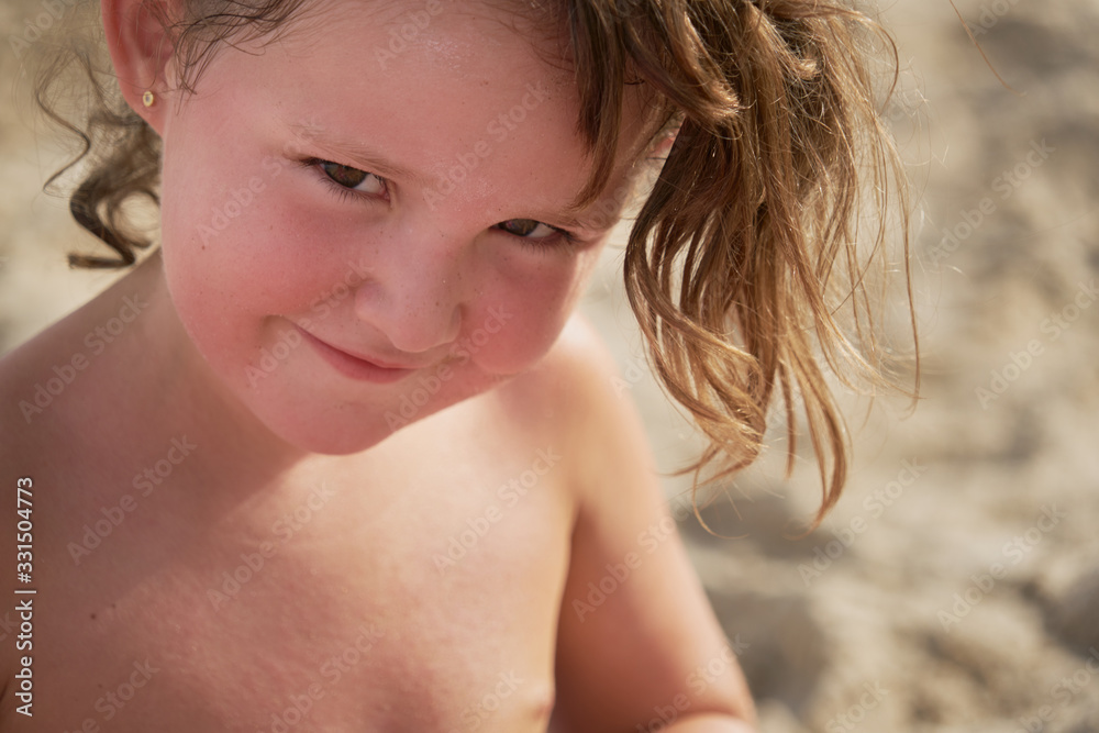 portrait of a smiling, happy caucasian girl on the beach looking out of the corner of her eye portrait of a smiling, happy caucasian girl on the beach looking out of the corner of her eye