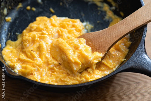 Scrambled eggs cooked in an cast iron skillet, wooden spatula.