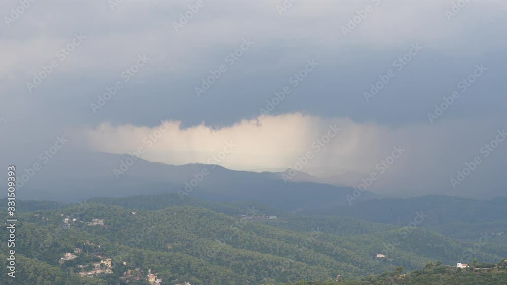 Rain over green mountains, heavy clouds and vertical precipitation shafts, small opening in middle. Telephoto view of rainstorm from distance, beautiful nature scene. Small buildings at green slope Rain over green mountains, heavy clouds and vertical precipitation shafts, small opening in middle. Telephoto view of rainstorm from distance, beautiful nature scene. Small buildings at green slope