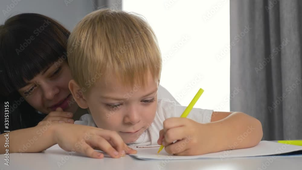 Happy family. Mom and son paint a picture in the album. Home schooling. Doing homework. Teamwork Happy family. Mom and son paint a picture in the album. Home schooling. Doing homework. Teamwork