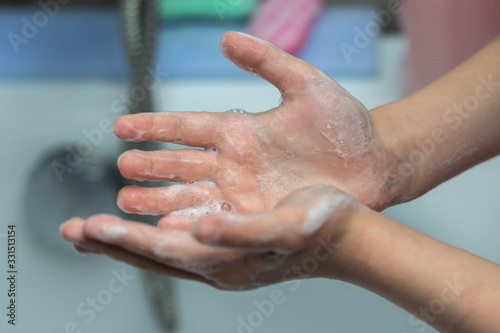 A child washes his hands in front of a faucet with water in the bathroom. Close-up