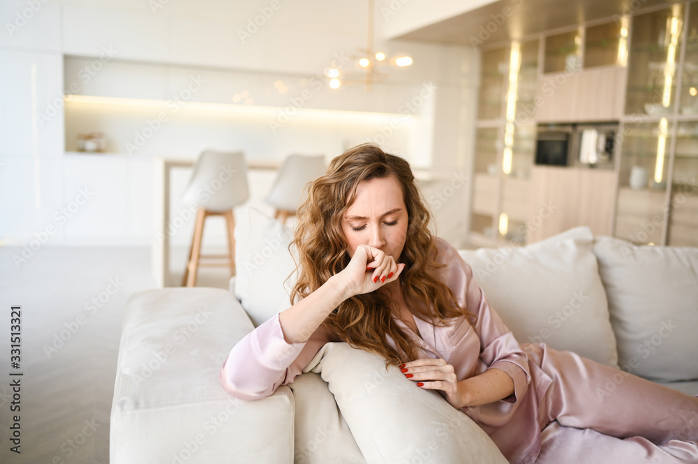 Coronavirus disease (COVID-19) symptoms - runny nose, sore throat, cough, fever. Young woman sick of flu viral infection spreading corona virus. Girl in pink pajamas lying in sofa at home quarantine Coronavirus disease (COVID-19) symptoms - runny nose, sore throat, cough, fever. Young woman sick of flu viral infection spreading corona virus. Girl in pink pajamas lying in sofa at home quarantine
