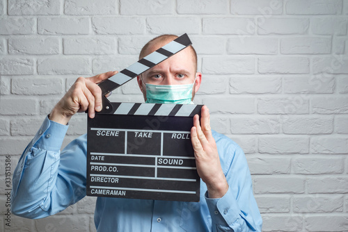 Man in blue shirt in virus mask on white with clapperboard