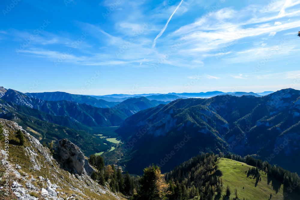 Naklejka premium A vast view on an Alpine valley in the region of Hochschwab, Austria. High mountain ranges surrounding the road in the valley. Soft morning haze. Exploration and achievment